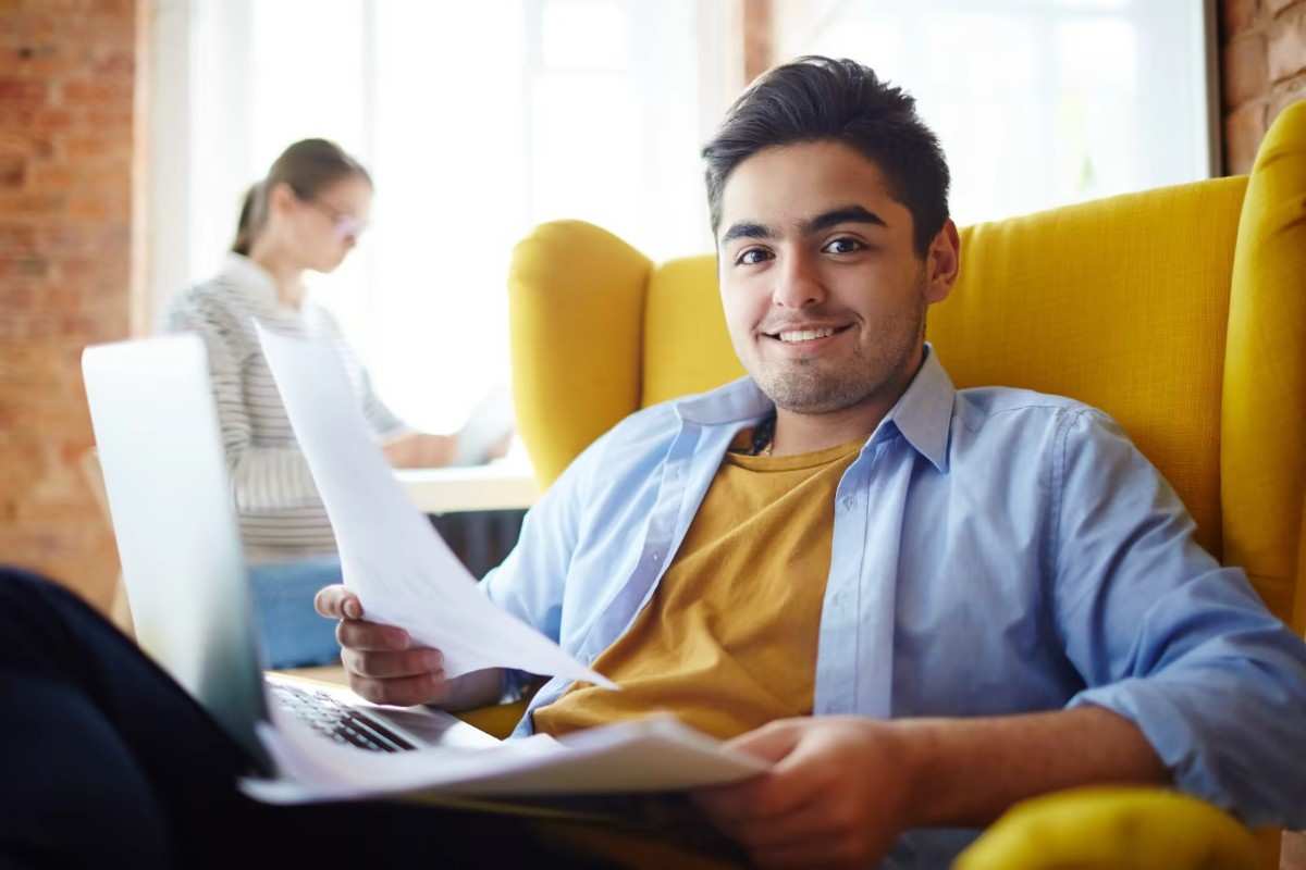 A young man with a lovely smile taking a paper while seated on a yellow sofa